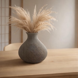 May include: A grey vase with a spiral design holds dried ornamental grass. The vase is on a wooden table, and the background is a neutral colour. The vase has a bulbous shape and a narrow neck.