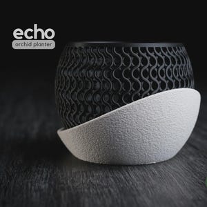 Puede incluir: Una maceta para orquídeas en blanco y negro con la etiqueta echo orchid planter. La sección superior presenta un patrón de celosía negro complejo y repetitivo en forma de ondas, mientras que la base es un cuenco blanco texturizado con un borde curvo.
