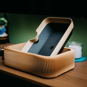 May include: A wooden box with a wavy, ribbed design. The box has a lid that is partially open, revealing a dark interior. The box is made of light brown wood and sits on a wooden surface.