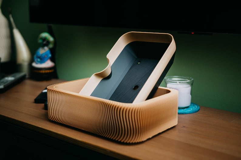 May include: A wooden box with a wavy, ribbed design. The box has a lid that is partially open, revealing a dark interior. The box is made of light brown wood and sits on a wooden surface.