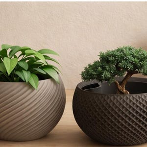 May include: Two decorative planters, one light brown with a spiral design and the other dark brown with a geometric pattern. The light brown planter holds a leafy green plant, while the dark brown one contains a small bonsai tree. Additional decor includes vases and folded linens.
