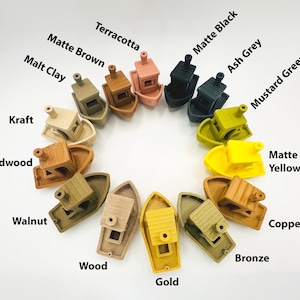 Pu&ograve; includere: Una collezione di modelli di barche in miniatura in vari colori, tra cui Terracotta, Nero Opaco e Oro. Ogni barca presenta una cabina e un fumaiolo. L'immagine include etichette di testo per ogni colore, come "Verde Senape" e "Giallo Opaco."