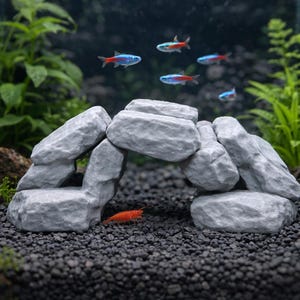 Może przedstawiać: Szara formacja skalna z łukiem, przeznaczona do akwarium. Kilka małych, kolorowych ryb z czerwonymi i niebieskimi oznaczeniami pływa nad skałami. Mała, pomarańczowa krewetka spoczywa na ciemnym podłożu żwirowym.