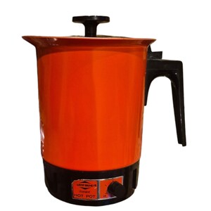 Op de afbeelding: Een feloranje West Bend instant HOT POT elektrische waterkoker met een zwarte handgreep, zwarte dekselknop en een zwarte voet met een temperatuurregelknop. Het label aan de voorzijde toont de tekst West Bend instant HOT POT.