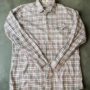May include: A long-sleeve button-down shirt featuring a plaid pattern in shades of white, dark red, and black. The shirt includes a standard collar, a single chest pocket on the left side, and a full-length front button closure with matching buttons.