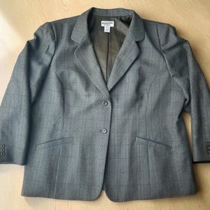 May include: A grey blazer with a subtle dark plaid pattern, featuring a notched lapel, two front buttons, and three smaller buttons on each sleeve cuff. The interior is lined with a solid olive-green fabric and includes a Pendleton brand label.