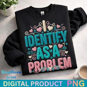 Puede incluir: Sudadera negra con el texto "I IDENTIFY AS A PROBLEM" en turquesa, rosa y blanco, con corazones y espirales decorativos. Las palabras "DIGITAL PRODUCT PNG" están en la parte inferior. Una taza de café está en el fondo.