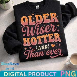 May include: Black sweatshirt with the text "OLDER, Wiser, HOTTER (AND) Than ever" in a retro font. The design includes orange, pink, and white lettering with star and heart accents. A digital product.
