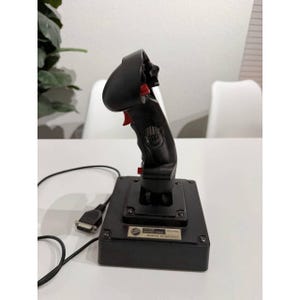 May include: A black joystick with red buttons and a base. The joystick has a curved handle and a series of buttons. A cable extends from the base. The joystick is designed for use with a computer or gaming system.