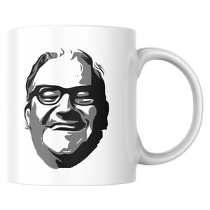 May include: White ceramic mug with a black and grey illustration of a man's face wearing spectacles. The mug has a curved handle on the right. The design is a simple, bold graphic.