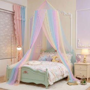 May include: A pastel rainbow-colored bed canopy made of sheer, flowing fabric draped from a circular ceiling mount. The canopy features integrated string lights and hangs over a light green bed frame with a floral motif and patterned bedding.