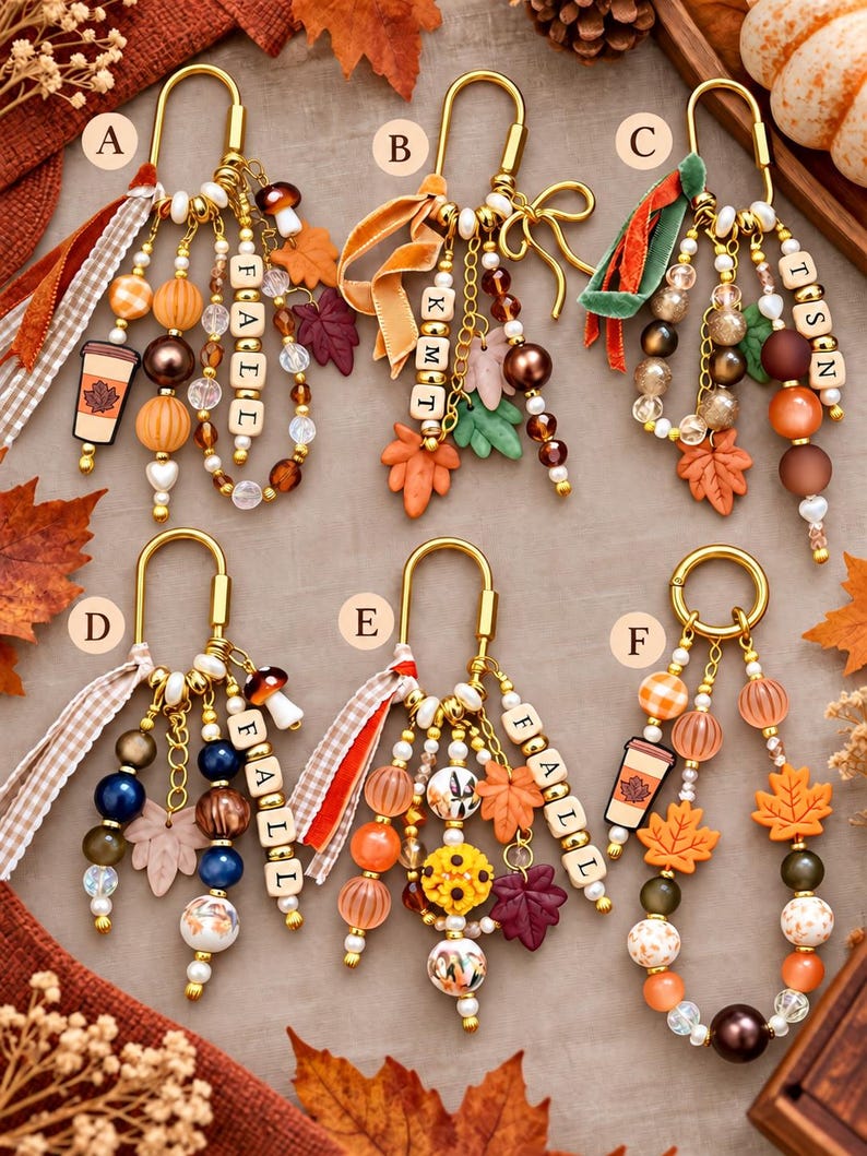 May include: Six gold-toned metal keychains labeled A through F, featuring assorted beads in orange, brown, and cream, fabric ribbons, and charms including maple leaves, mushrooms, and coffee cups. Some keychains include lettered wooden beads.