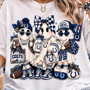 May include: A white t-shirt featuring a graphic of three ghosts wearing blue and white Indianapolis Colts themed apparel, including hats, bows, sunglasses, and sneakers, with accessories like a tote bag, a football, and a pom-pom.