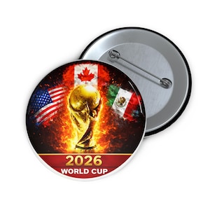 Può includere: Un bottone rotondo con retro argento e spilla. Presenta il trofeo della Coppa del Mondo FIFA circondato da fiamme, con le bandiere di USA, Canada e Messico. Il testo "2026 WORLD CUP" è visibile.