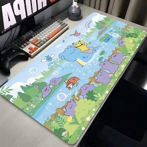 Könnte beinhalten: Rechteckige Schreibtischunterlage mit einer bunten Cartoon-Szene mit Fluss, Bäumen und verschiedenen animierten Charakteren. Die Unterlage hat einen blauen Hintergrund mit einem Regenbogen.