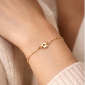 Peut inclure: Un bracelet doré délicat orné d'un charm en forme de soleil. Le charm est un petit motif de soleil détaillé. Le bracelet est porté sur un poignet, et la chaîne est fine et élégante. Le bijou est un accessoire simple mais élégant.