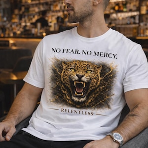 May include: White t-shirt featuring a snarling leopard graphic with the text "NO FEAR. NO MERCY." above and "RELENTLESS" below. The leopard has yellow eyes and is surrounded by lightning bolt designs.