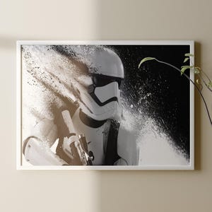 Könnte beinhalten: Gerahmter Druck mit einem Stormtrooper aus Star Wars in Schwarzweiß. Das Bild hat einen dynamischen, künstlerischen Effekt. Der Stormtrooper ist in seiner weißen Rüstung mit einem Blaster dargestellt. Der Hintergrund ist dunkel mit einem weißen, strukturierten Effekt.