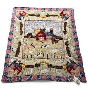May include: A rectangular quilt featuring a central farm scene with a red barn, a yellow sun, a horse, a cow, a sheep, and various poultry. The border is decorated with alternating blue and pink patterned squares and farm motifs.