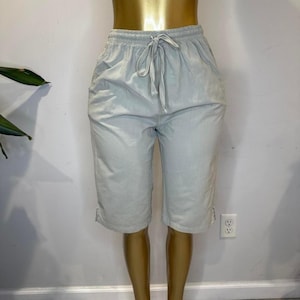 Puede incluir: Pantalones capri de color gris claro con cintura elástica y cordón. Los capris tienen bolsillos y se exhiben en un maniquí. Los capris son hasta la rodilla y tienen un estilo casual.