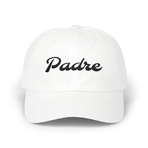 May include: White baseball cap with the word "Padre" in black script across the front. The cap has a curved brim and a rounded crown. The hat is made of a soft material.