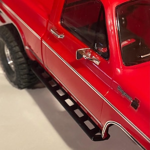 Pode incluir: Um close-up de um caminhão de brinquedo vermelho com pneus pretos e um estribo preto. O caminhão tem espelhos laterais e acabamentos cromados. A palavra "Cheyenne" é visível na lateral do caminhão.
