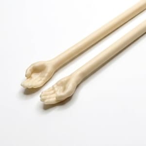 Puede incluir: Dos objetos alargados de color crema con extremos en forma de mano. Las manos están abiertas, con dedos y palmas visibles. Los objetos están colocados en diagonal sobre un fondo blanco, lo que sugiere un artículo decorativo o artístico.