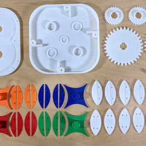May include: A collection of white plastic toy parts, including gears, oval shapes, and connecting pieces, laid out on a light wood surface. The components are ready for assembly.
