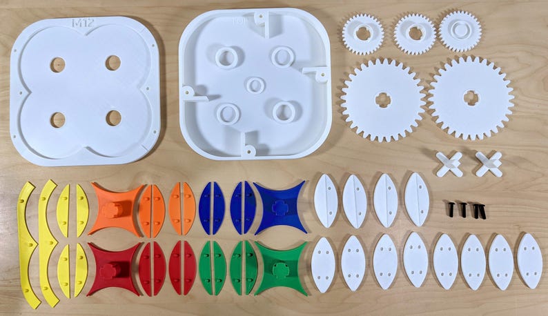 May include: A collection of white plastic toy parts, including gears, oval shapes, and connecting pieces, laid out on a light wood surface. The components are ready for assembly.