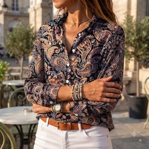 Könnte beinhalten: Ein langärmeliges Hemd mit Knopfleiste und einem mehrfarbigen Paisley-Muster auf dunkelblauem Grund in Orange-, Beige- und Violetttönen. Das Hemd wird mit einer weißen Hose und einem braunen Ledergürtel mit goldfarbener Metallschnalle kombiniert.