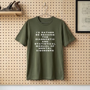 Peut inclure: Une tasse en céramique blanche avec une anse noire et le texte "But First, Coffee" en noir, dans une police manuscrite. La tasse est posée sur une surface blanche.