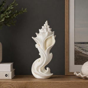 May include: A white seashell sculpture with a detailed, swirling design. The decorative piece has a textured surface and is placed on a wooden shelf. The sculpture is a coastal-themed home decor item.