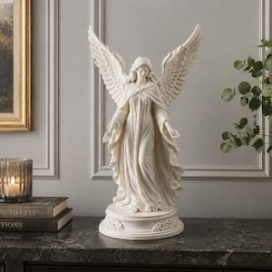 Könnte beinhalten: Eine cremefarbene Engelsstatue mit einer Figur, die große, detaillierte Flügel weit ausgebreitet hat und ein langes, fließendes Gewand mit drapiertem Stoff trägt. Die Skulptur steht auf einem runden Sockel mit floralen Verzierungen.