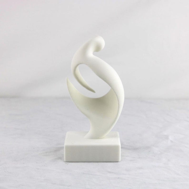 May include: A white abstract sculpture featuring a smooth, curved, and fluid form that rises from a solid square base. The object has a matte finish and consists of interconnected, sweeping lines that create an open, hollow center.