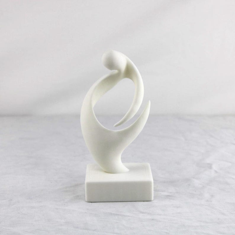 May include: A white abstract sculpture featuring a smooth, curved, organic form that loops upward from a solid square base. The piece has a matte finish and consists of continuous, flowing lines that create an open, negative space in the center.
