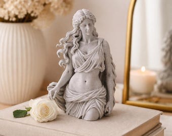 May include: A light gray stone-textured bust sculpture of a figure with long flowing hair, wearing a draped garment that leaves the midriff exposed. The figure is depicted in a standing pose with one hand resting near a single white rose blossom.