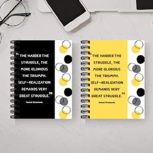 May include: Two spiral-bound notebooks, one black and one yellow, with the quote "The harder the struggle, the more glorious the triumph." The notebooks have a design of circles and are on a white surface with office supplies.