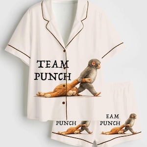 Puede incluir: Conjunto de pijama blanco con ribete marr&oacute;n, con un gr&aacute;fico divertido de un mono golpeando un peluche. Las palabras "TEAM PUNCH" est&aacute;n impresas en la camisa, y "PUNCH" y "EAM PUNCH" en los pantalones cortos.