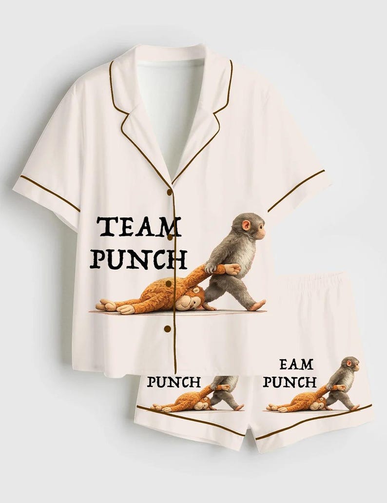 Puede incluir: Conjunto de pijama blanco con ribete marr&oacute;n, con un gr&aacute;fico divertido de un mono golpeando un peluche. Las palabras "TEAM PUNCH" est&aacute;n impresas en la camisa, y "PUNCH" y "EAM PUNCH" en los pantalones cortos.