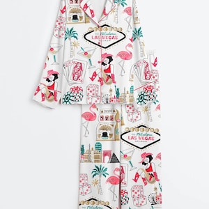 May include: White pajama set with a Las Vegas theme. The set features a button-down top and pants, adorned with illustrations of flamingos, dice, playing cards, cocktails, and the text "To Fabulous Las Vegas Nevada."