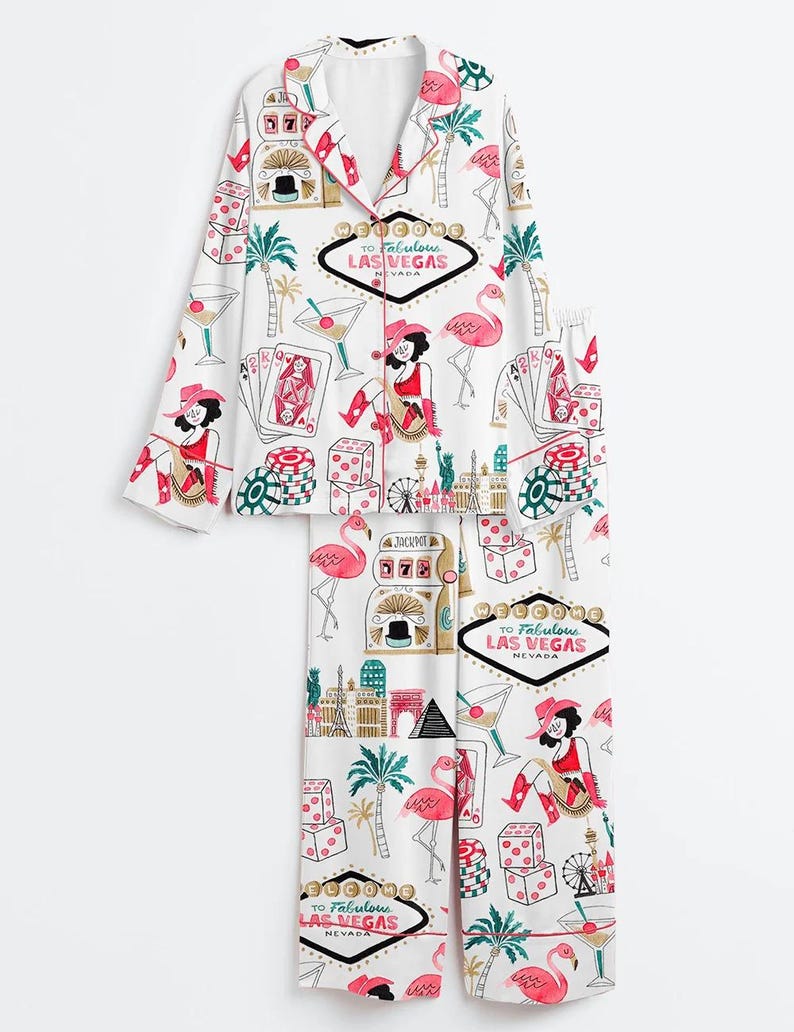 May include: White pajama set with a Las Vegas theme. The set features a button-down top and pants, adorned with illustrations of flamingos, dice, playing cards, cocktails, and the text "To Fabulous Las Vegas Nevada."