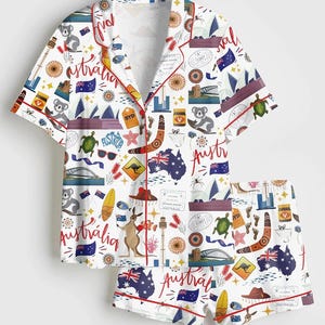May include: White pajama set with an Australian theme. The short-sleeved top and shorts feature a repeating pattern of Australian icons, including kangaroos, koalas, flags, and landmarks, with red trim.