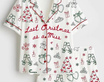 May include: A white short-sleeve button-down pajama shirt and matching shorts set with red piping. The fabric features a repeating print of Christmas trees, gingerbread men, champagne flutes, rings, and snowflakes, with the text Last Christmas as a Miss.