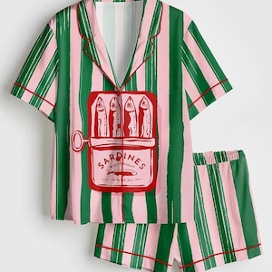 May include: A two-piece pajama set featuring a green and pink striped pattern. The top has a red-trimmed collar and a sardine can graphic. The shorts also have the same striped pattern and red trim. The pajamas are made of a soft, comfortable material.