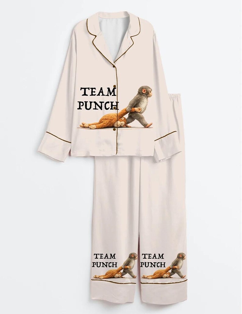 Puede incluir: Conjunto de pijama rosa claro con una camisa con botones y pantalones a juego. La camisa y los pantalones presentan el texto "TEAM PUNCH" y un gr&aacute;fico de un mono que lleva a otro mono. El pijama tiene ribetes marrones.