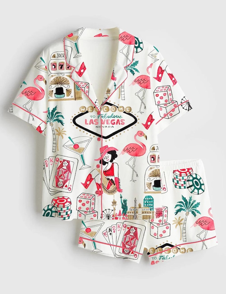 May include: White pajama set with a Las Vegas theme. The short-sleeved top and shorts feature a print of flamingos, dice, playing cards, and the text "Welcome to Fabulous Las Vegas Nevada". The set has red trim.