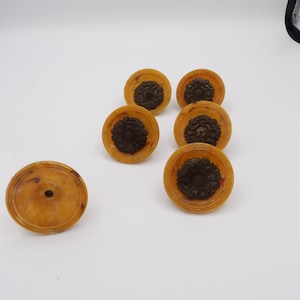 May include: A set of six circular furniture knobs featuring a translucent amber-colored base with a marbled pattern and a dark brown, ornate, floral-shaped metal center inlay. Each knob has a smooth, rounded edge and a central mounting hole.