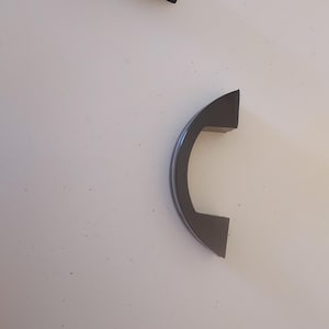 May include: Two arched cabinet handles featuring a glossy black finish with a central silver-toned metallic stripe running along the curve. Each handle has two mounting points at the ends, designed for attachment to furniture or cabinetry doors.