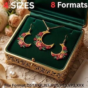 Puede incluir: Un conjunto de joyería que incluye un colgante de media luna dorada y pendientes a juego, decorados con flores bordadas en rojo y rosa con hojas verdes. El conjunto se presenta en una caja forrada de terciopelo verde con texto.