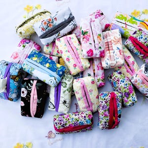 May include: A selection of fabric tissue box covers in diverse floral and patterned designs. The covers display a variety of colours, including pink, blue, yellow, and black. Each cover has a rectangular shape with a slit for tissue dispensing.
